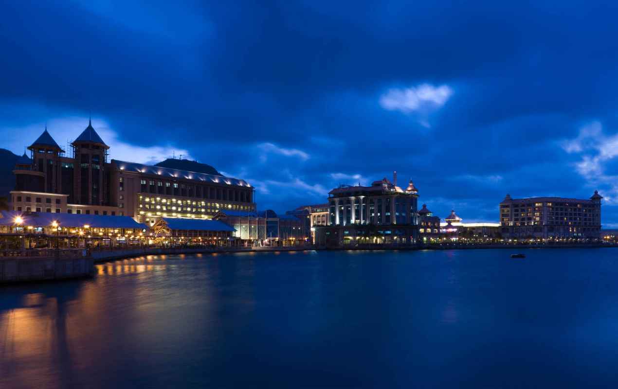 Buildings at the waterfront lit up at dusk, Caudan Waterfront, Port Louis, Mauritius
